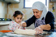 © Anastasia - A senior Middle Eastern woman teaches a young girl to knead dough in a cozy kitchen, showcasing tradition and togetherness through cooking and shared moments