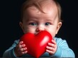 © Татьяна Кузнецова - Cute baby holds red heart symbolizing love and affection in a soft-lit indoor setting, showcasing innocence and joy during a playful moment