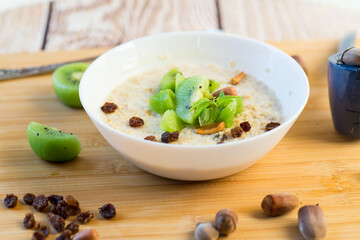 Wall Mural - cooked oatmeal with kiwi, honey and nuts in a bowl on a wooden table