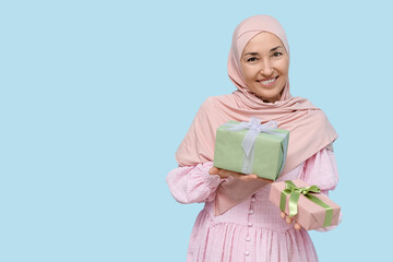 Wall Mural - Mature Muslim woman with gift boxes on blue background. International Women's Day