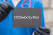 © wladimir1804 - Doctor holding black cardboard card with text: COXSACKIEVIRUS. Coxsackievirus research treatment health care concept. Coxsackieviruses contagious enterovirus genus. Coxsackie virus.