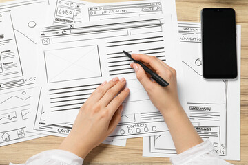 Wall Mural - website designer creating wireframe on paper with pen at wooden table, top view