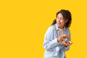 Poster - African-American woman with tasty eclairs on yellow background