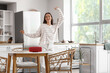 © Pixel-Shot - Beautiful young happy woman with wireless portable speaker in kitchen at home