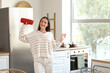 © Pixel-Shot - Beautiful young happy woman with wireless portable speaker in kitchen at home