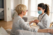 © Dorde - Caucasian female doctor wearing white coat and protective mask provides compassionate medical care to senior patient during professional home healthcare visit.