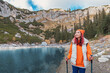 © EdNurg - Female hiker with trekking poles enjoying stunning view of mountain lake and cliffs during autumn hike