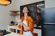 © SHOTPRIME STUDIO - Young woman in orange shirt enjoying a healthy green drink in a modern kitchen, radiating happiness and wellness, vibrant colors, bright interior design