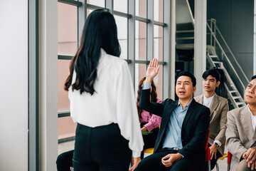 Wall Mural - In the midst of a conference, a young man eagerly raises his hand to pose a question. The group exemplifies collaborative teamwork and animated discussion, encouraging active learning.