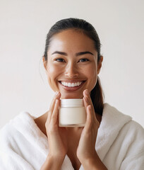 Wall Mural - Smiling young Asian woman wearing bathrobe and holding cosmetic cream