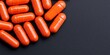 © Jeannaa - drug assessment compliance concept. Close-up of orange capsules on a textured black surface.