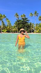 Poster - Clear waters beckon as a woman traveler wades through the stunning beaches of Koh Kood. Surrounded by lush palm trees, the tropical escape promises blissful relaxation under the sun.