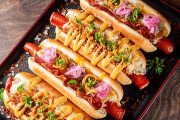 Wall Mural - A tempting platter of gourmet hot dogs topped with crispy bacon, creamy mustard, pickled onions, and fresh herbs. Perfect for food lovers seeking indulgent street-style snacks.