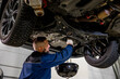 © AvokadoStudio - A working car mechanic unscrews the drain plug of the crankcase on the pallet to drain and replace the engine oil