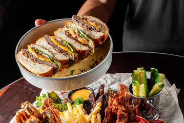 Wall Mural - A delicious meal featuring a stacked sandwich with juicy patties, lettuce, and sauces, served alongside fries, pickles, and tasty sides, perfect for a food lover's delight.