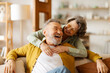 © Home-stock - Loving romantic senior couple enjoying their relationships and long lasting marriage, woman embracing her husband while man sitting on sofa