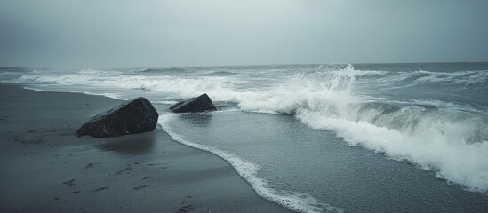 Leinwandbilder - Waves crashing on rocky beach under overcast skies with gray sand creating a serene coastal atmosphere