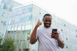 © Юлия Завалишина - Happy African American man euphoric winner with smartphone on street in city. Person guy looking at cell phone reading great news getting good result winning online bid feeling amazed. Winning gesture