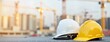 © Pete - Safety equipment for construction workers. Two hard hats rest on grey surface. Blurred background shows construction site with cranes. Hard hats white, yellow. Photo useful for construction