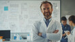 © Aloka - A smiling doctor in a lab coat with crossed arms, standing in front of a whiteboard filled with medical diagrams, surrounded by other engaged researchers. Ai generated