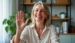 © Pete - Mature woman smiles, waves at webcam. Happy teacher counselor in video chat. Remote online communication. Home office setting. Professional attire. Distance learning support session. Happy expression.