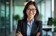 © Pete - Successful Asian businesswoman stands confidently in modern office. She wears business suit and smiles warmly. This confident professional radiates success and leadership in contemporary workplace.