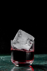 Wall Mural - A close-up of an elegant glass filled with a deep red beverage and a large ice cube, set against a dark background. The scene captures the refreshing and inviting essence of a cocktail.