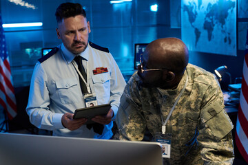 Aufkleber - Serious mature male officer in uniform looking at young African American colleague bending over computer monitor
