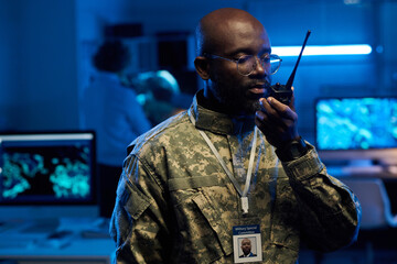 Aufkleber - Young African American man in eyeglasses and camouflage uniform speaking in walkie-talkie in front of camera