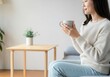 © Sandor - Serene moment of a young woman savoring a hot drink in her comfortable living room, enjoying a peaceful atmosphere