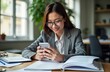 © Viktor - Smiling Asian businesswoman uses smartphone in office. Pro female executive browses tech app on mobile. Happy lady works at desk in modern office environment. Businesswoman looks happily at mobile