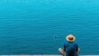 © Duskcraft - Young Man Sitting by Tranquil Water Wearing Straw Hat and Blue Shirt