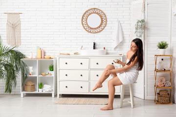 Wall Mural - Young woman applying cream on her leg after shower in bathroom