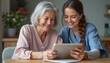 © kotlyarn - A smiling elderly woman and a young female caregiver share a moment of joy as they look at a tablet together. This heartwarming scene captures the essence of companionship and the positive impact of