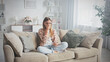 © MIKHAIL - Sad woman sitting on the sofa in the living room, crying and covering her face with her hand while reading a distressing message on her smartphone, overwhelmed by negative emotions