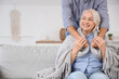 © Pixel-Shot - Young man covering his mother with warm plaid on sofa at home