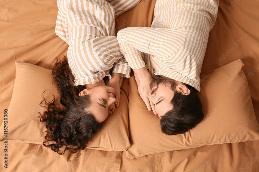 Happy couple in pajamas lying on bed, top view