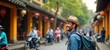 © Viktor - Happy solo traveler enjoys sightseeing in Hoi Ancient town Vietnam. Man with backpack, hat walks along street. Colorful buildings, lanterns line street. Many people around street. Vacationing in
