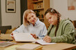 © AnnaStills - Mature mother sitting at table in living room, helping her daughter with disability to do homework for school