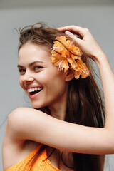 Wall Mural - Cheerful young model with flower in hair, wearing vibrant attire, showcasing joy against a soft background, perfect for seasonal beauty themes.