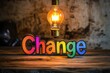 © Sean Hoong - The word 'Change' written in rainbow-colored letters on a rustic wooden table, with a bright light bulb shining above, symbolizing innovation and inspiration.