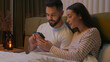 © Yuliia - Caucasian couple man woman husband wife boyfriend girlfriend together watching movie mobile phone smartphone gadget online internet browse networking glued stuck addict bed bedroom home interested web