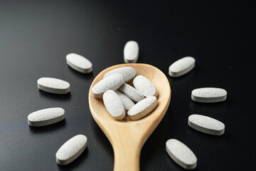 Wall Mural - white Pills Medicine tablet capsules in a wooden spoon blister pack on a black background