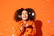 © VISTA by Westend61 - Smiling woman blowing confetti in front of orange background