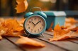 © Mitchell - Daylight Saving Time. Alarm clock and orange color leaves on wooden table. Autumn time. Fall time change. Autumn leaves fall and winter approaches- the concept of daylight saving time