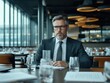 © Sergey - A confident man in a suit sits in a modern conference room with large windows and glassware around, exuding professionalism and focus.