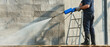 © Wonderful Studio - Concrete construction. A person using a pressure washer on a wall from a ladder.