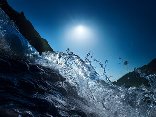 Poster - A powerful ocean wave crashes, sunlight glistening on the water's surface, creating a dramatic splash and spray against a deep blue sky and dark coastline.