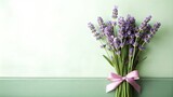 Bouquet of fresh lavender flowers tied with a pink ribbon on a soft green background, symbolizing tranquility and beauty, with copy space