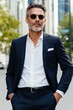 © Iryna - A man in a suit and sunglasses stands on a sidewalk. He is wearing a black suit jacket and a white shirt